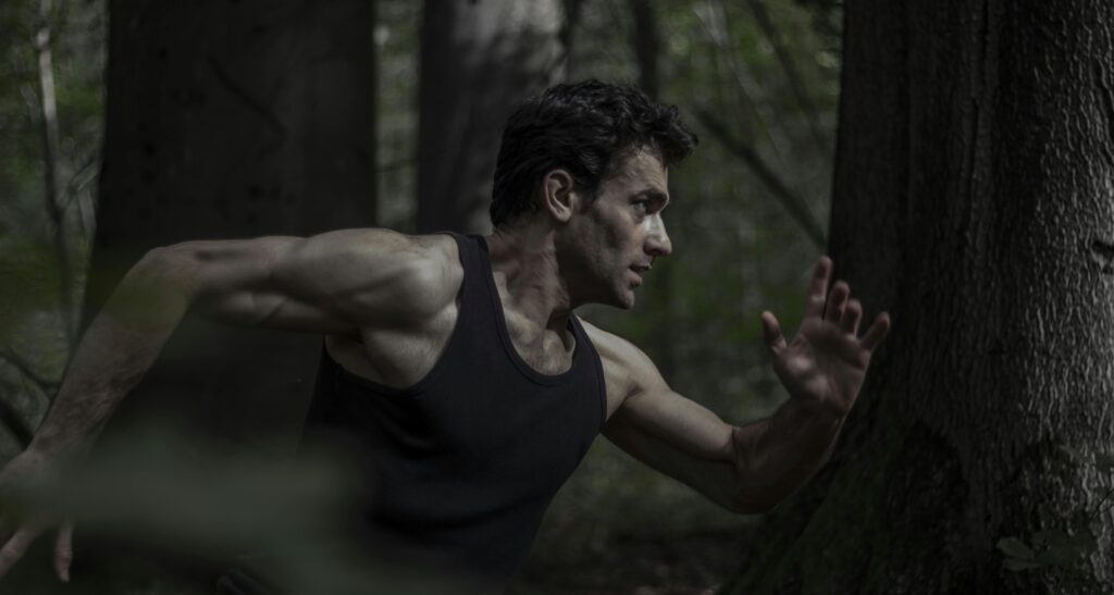 Athletic man in motion running through a dense forest, showcasing strength and energy.
